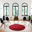 Foto: Großer hoher Raum mit weißen Wänden und 3 hohen Fenstern mit Rundbogen im Hintegrund. Im Vordergrund, mittig im Zimmer 5 Stühle auf Parkett im Halbkreis um roten Teppich.