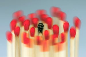 Foto: ca. 20 rote Steichholzkuppen an vertikal ausgerichteten Steichhölzern bewegen sich kreisförmig (bewegungsunschärfe) um einen mittig angeordneten abgebrannten Streichholz.